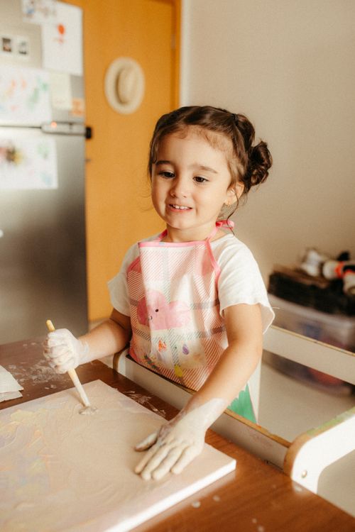 Free Young girl painting indoors with a smile, showcasing creativity and joy in a home setting. Stock Photo