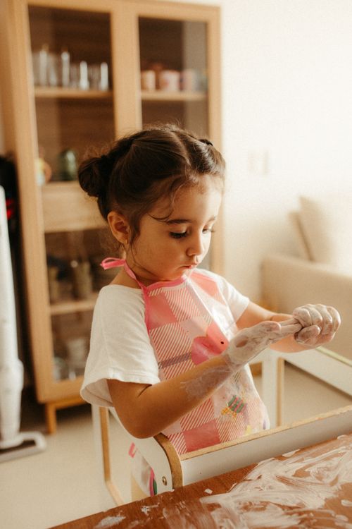 Free Young child enjoying creative play at home, wearing apron and using play dough. Stock Photo