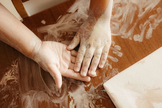 Child's hands covered in paint on a wooden table, exploring art playfully.