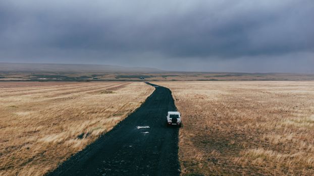 A lone vehicle on a rugged road in Iceland's vast, overcast landscape.