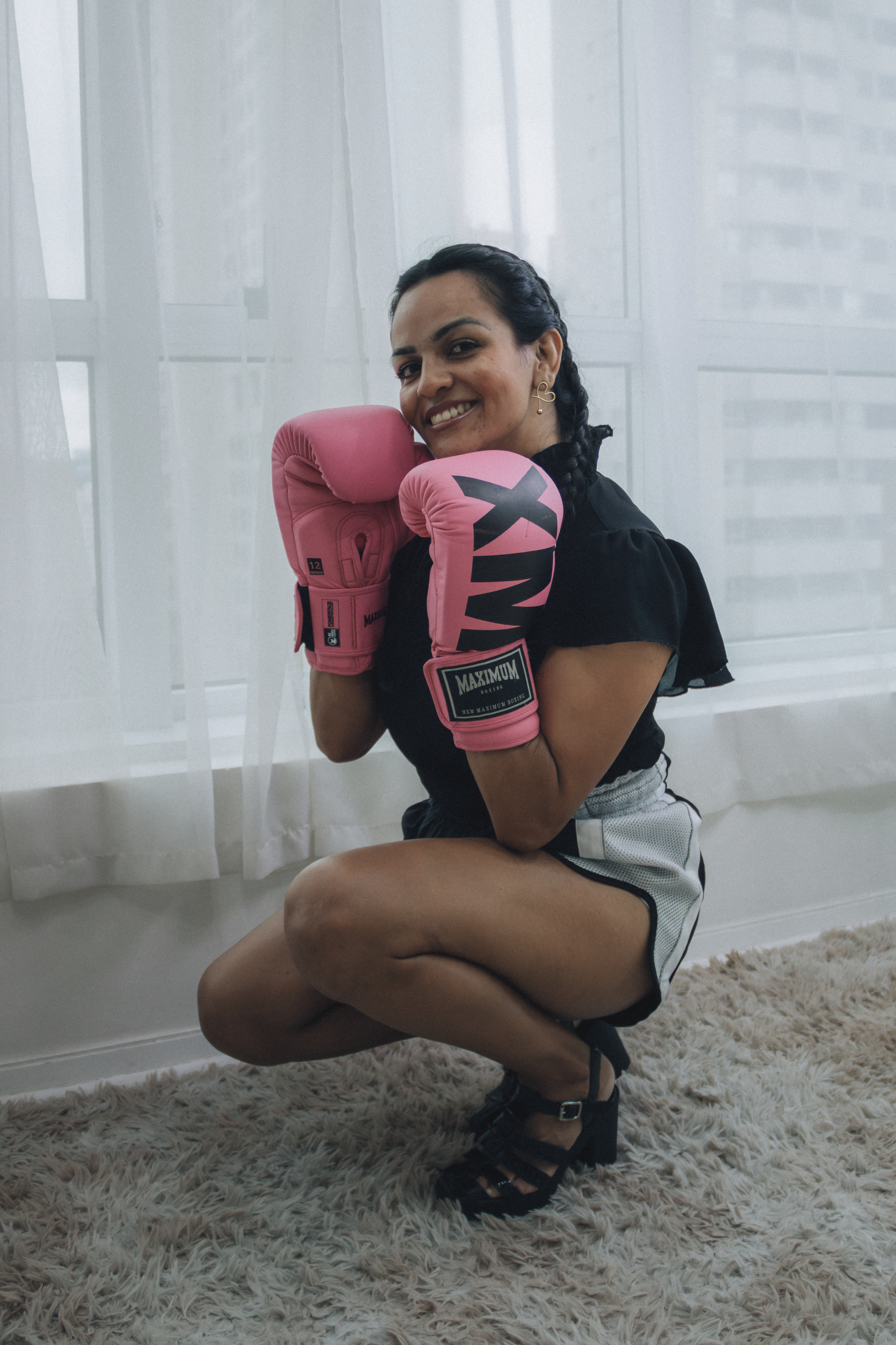 Confident woman with boxing gloves poses indoors, exuding strength and happiness.