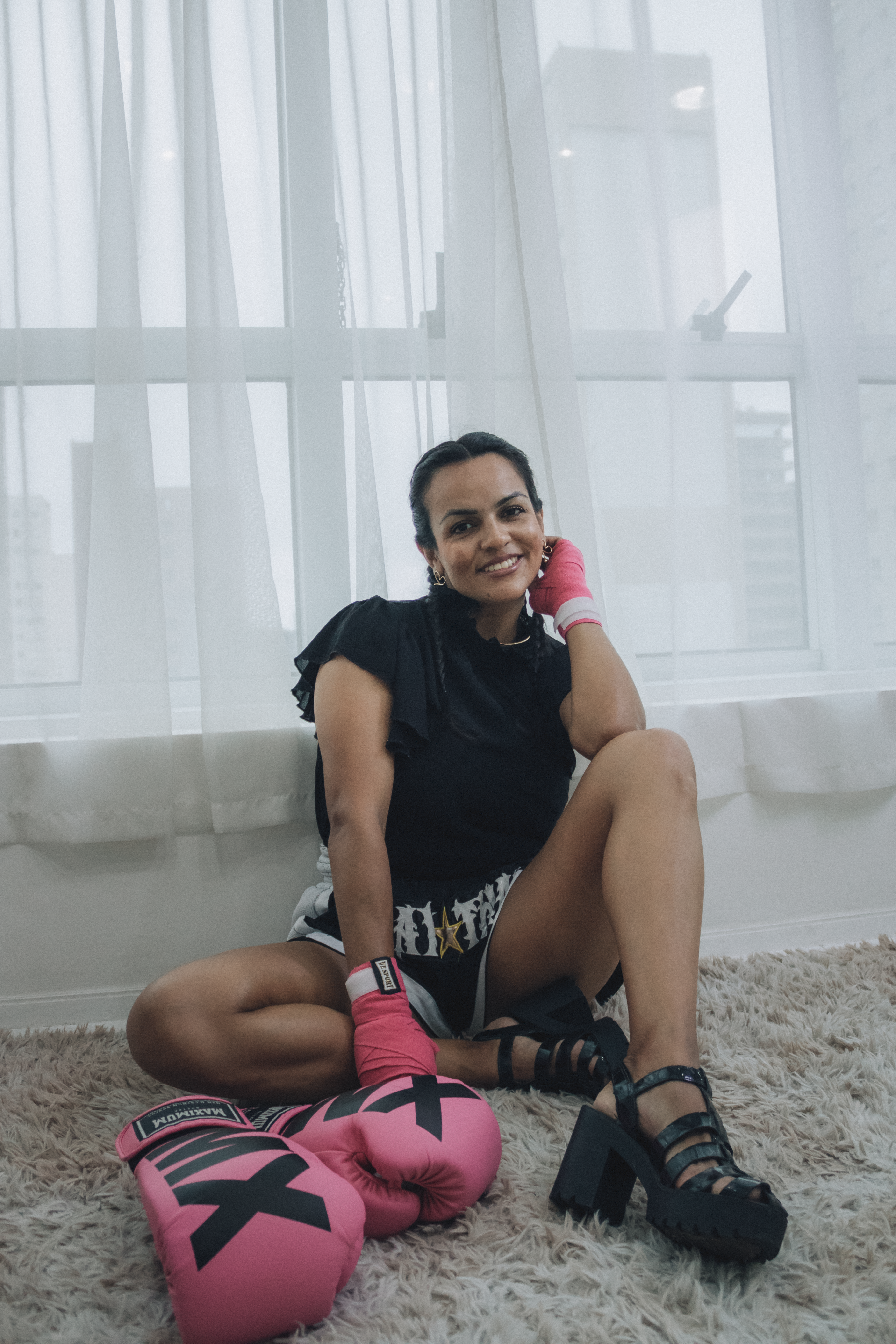 Confident woman with pink boxing gloves sitting indoors, smiling warmly.