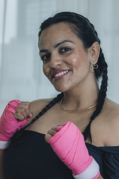 Portrait of a smiling female boxer with pink hand wraps, ready for action indoors.