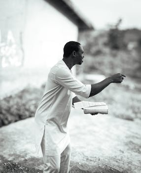 Black and white photo of an African preacher energetically giving a sermon outdoors.