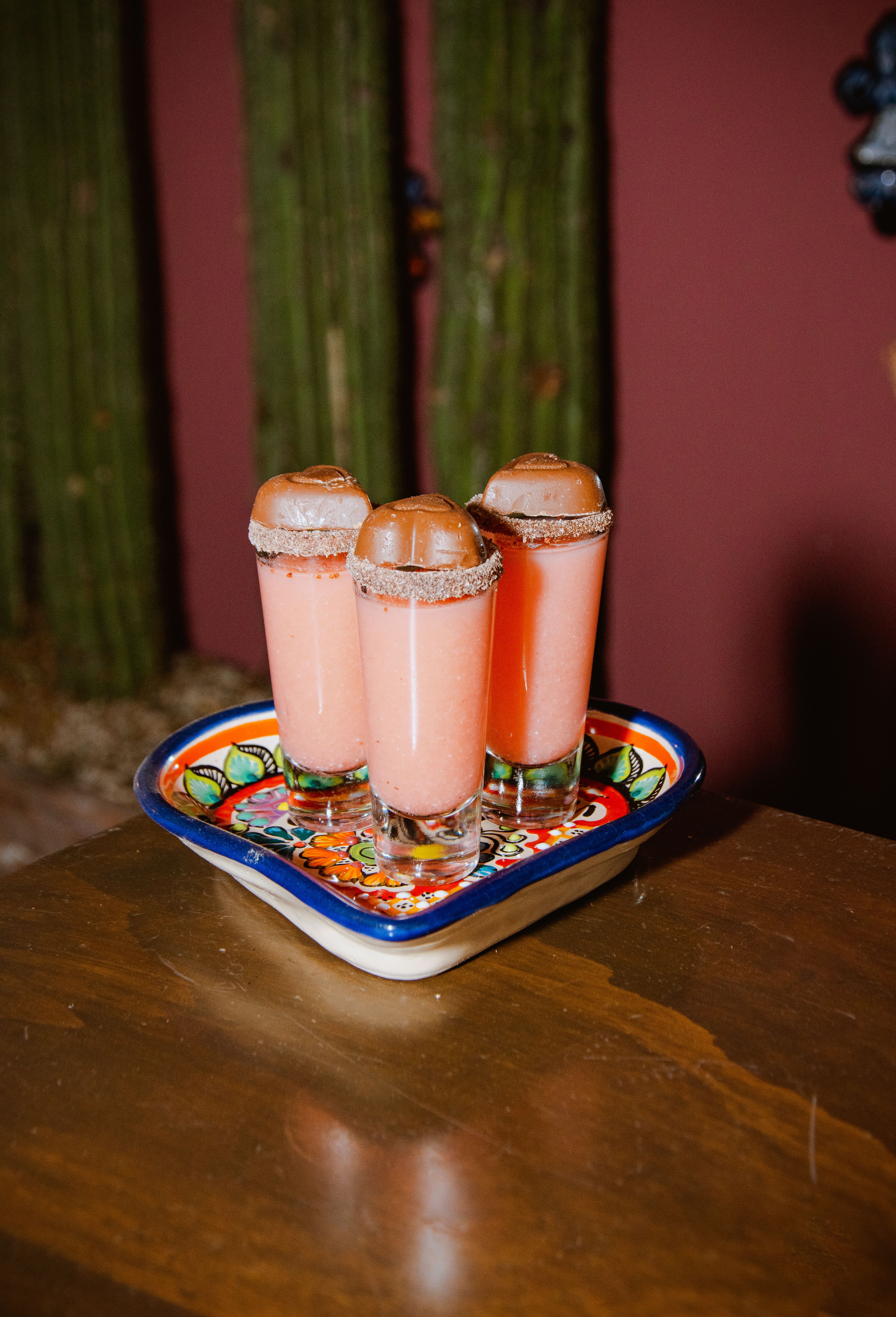 Colorful Mexican-themed shots with frothy pink drinks on a traditional tray.