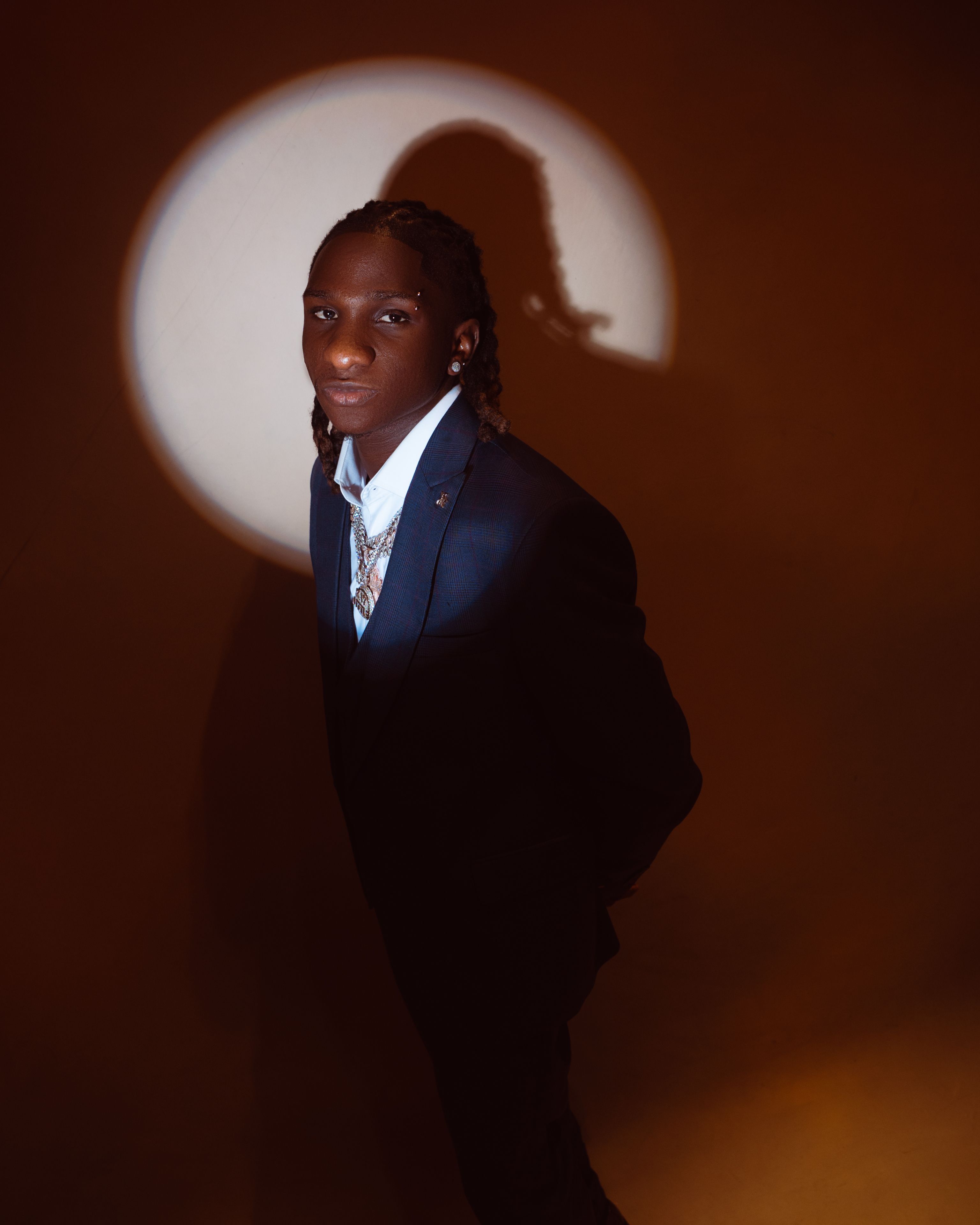 Stylish man in a suit illuminated by circular spotlight, creating a dramatic effect.