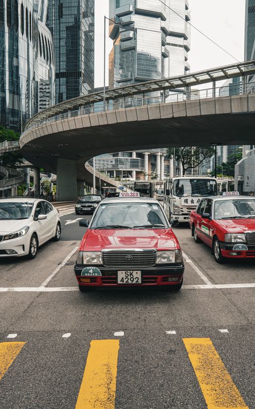 Free Red taxi amidst traffic and modern architecture in Hong Kong cityscape. Stock Photo