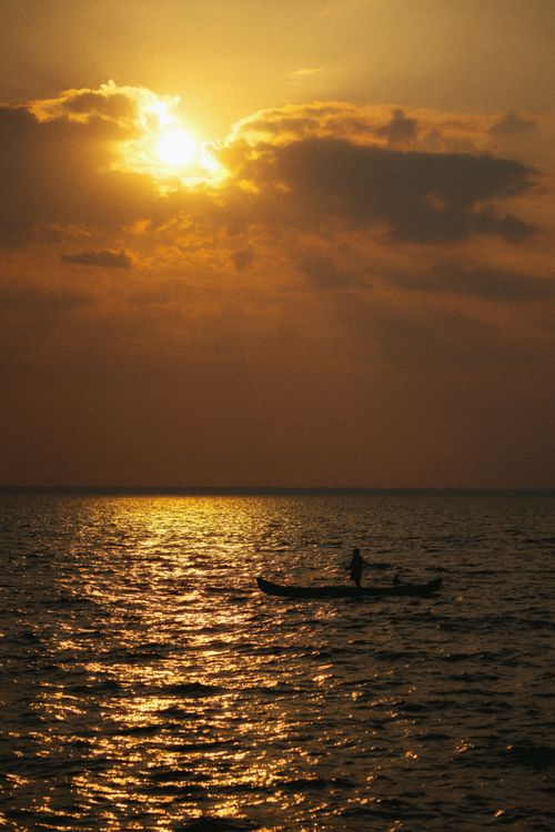 Free A lone person in a boat silhouetted against a golden sunset over the ocean in KL, India. Stock Photo