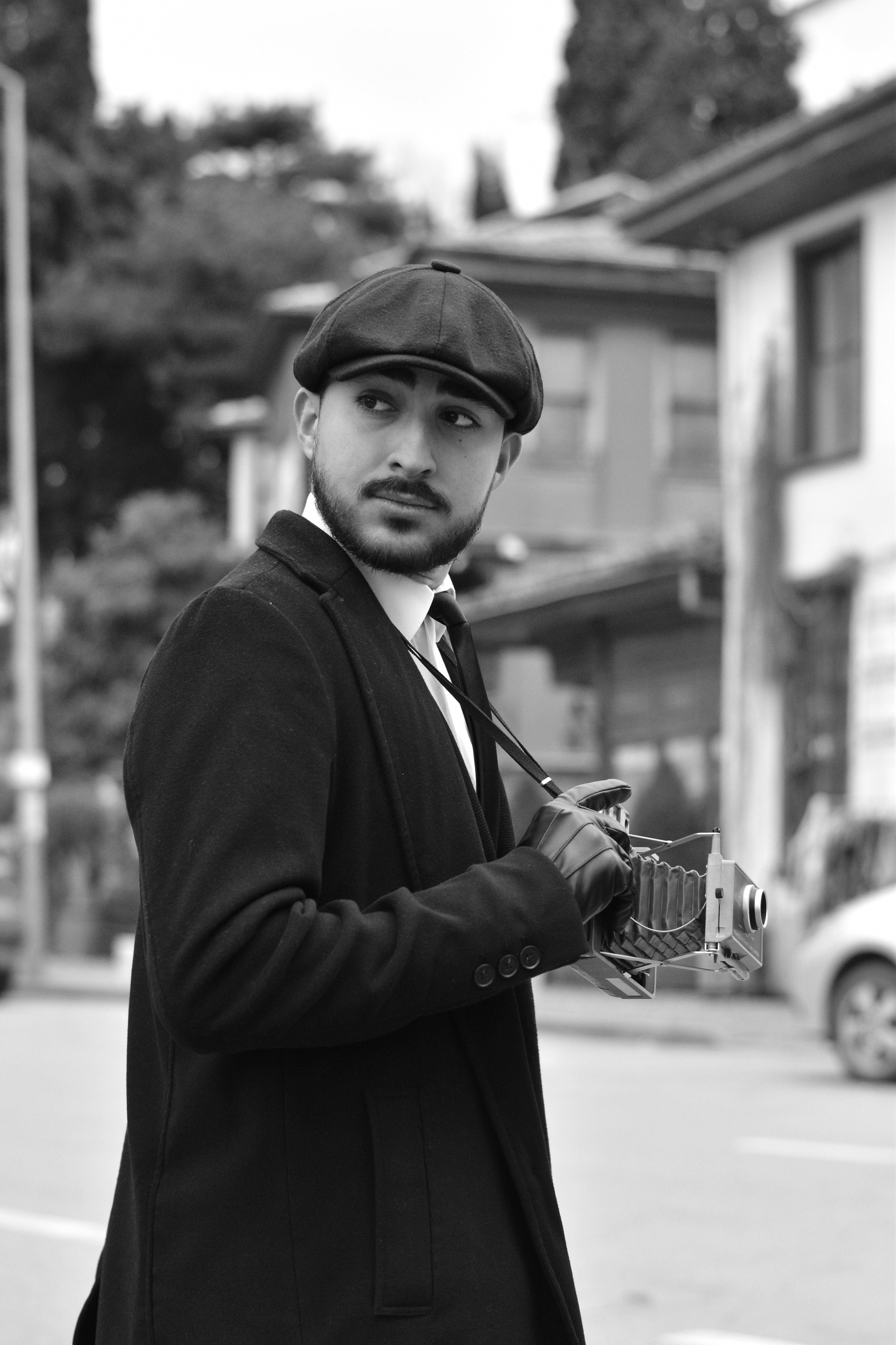 Black and white portrait of a man in vintage attire holding a retro camera, set in Bursa streets.