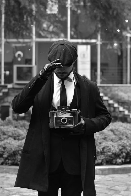 Free Black and white portrait of a man holding a vintage camera outdoors, dressed in retro attire, creating a timeless scene. Stock Photo
