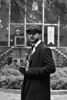 A man dressed in vintage style with a camera in hand outdoors.