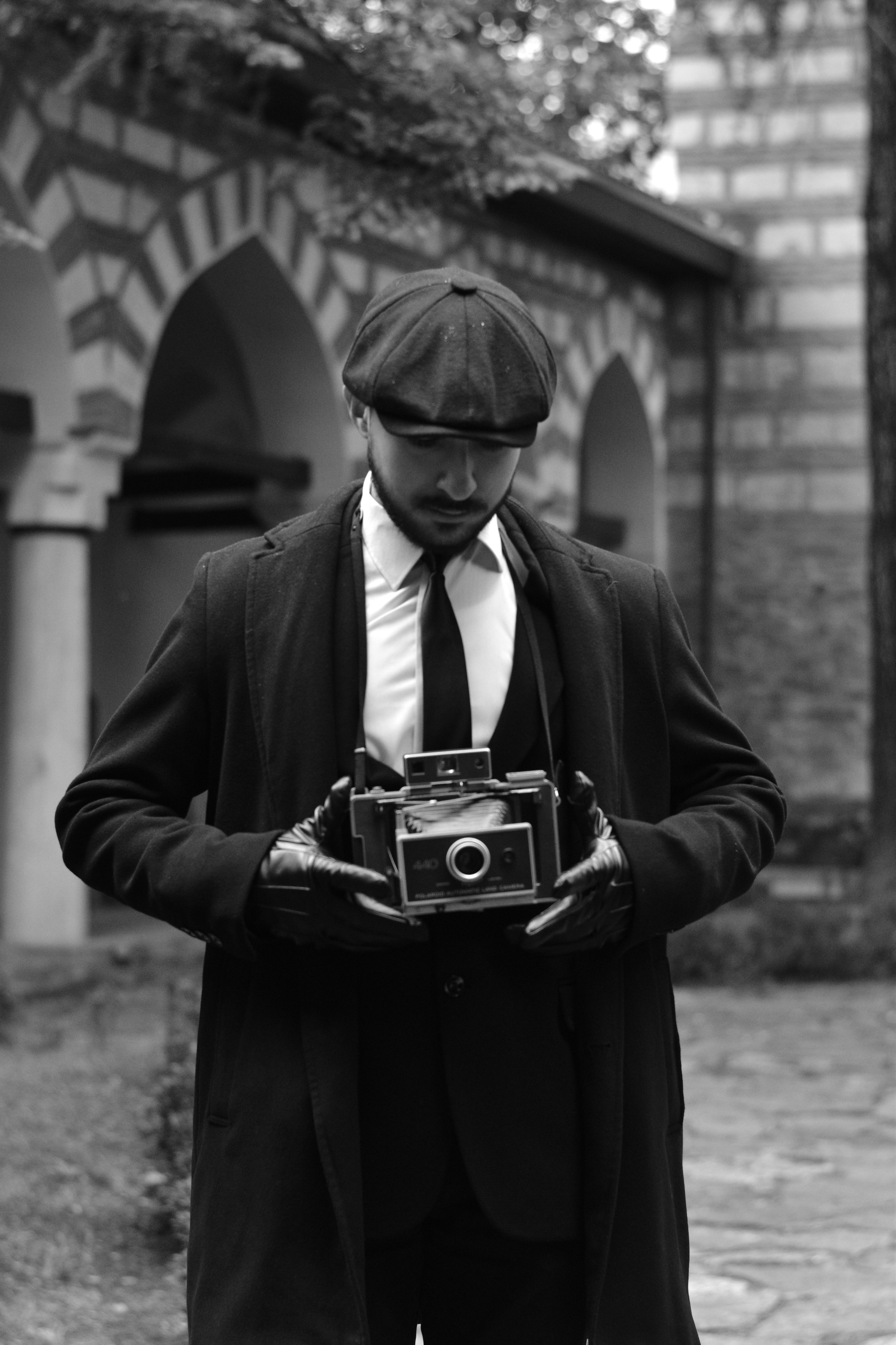 Black and white photo of a man in vintage attire holding a camera in a historic courtyard in Bursa, Türkiye.