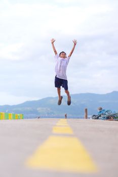 A joyful boy leaping into the air on a yellow-lined path with a scenic mountain backdrop.