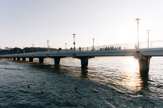 Silhouetted people walking along Kolberg Pier during a serene sunset over the water.
