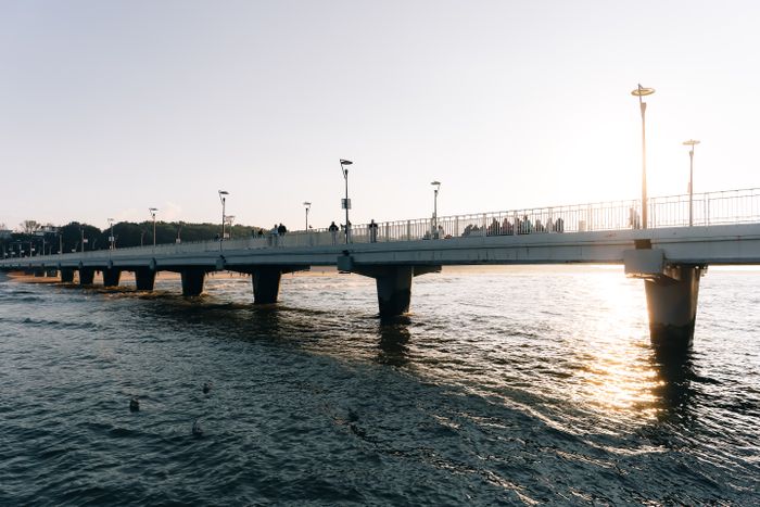 Figures walking a pier silhouetted against a low sun &mdash; photo by Riedelmax on Pexels