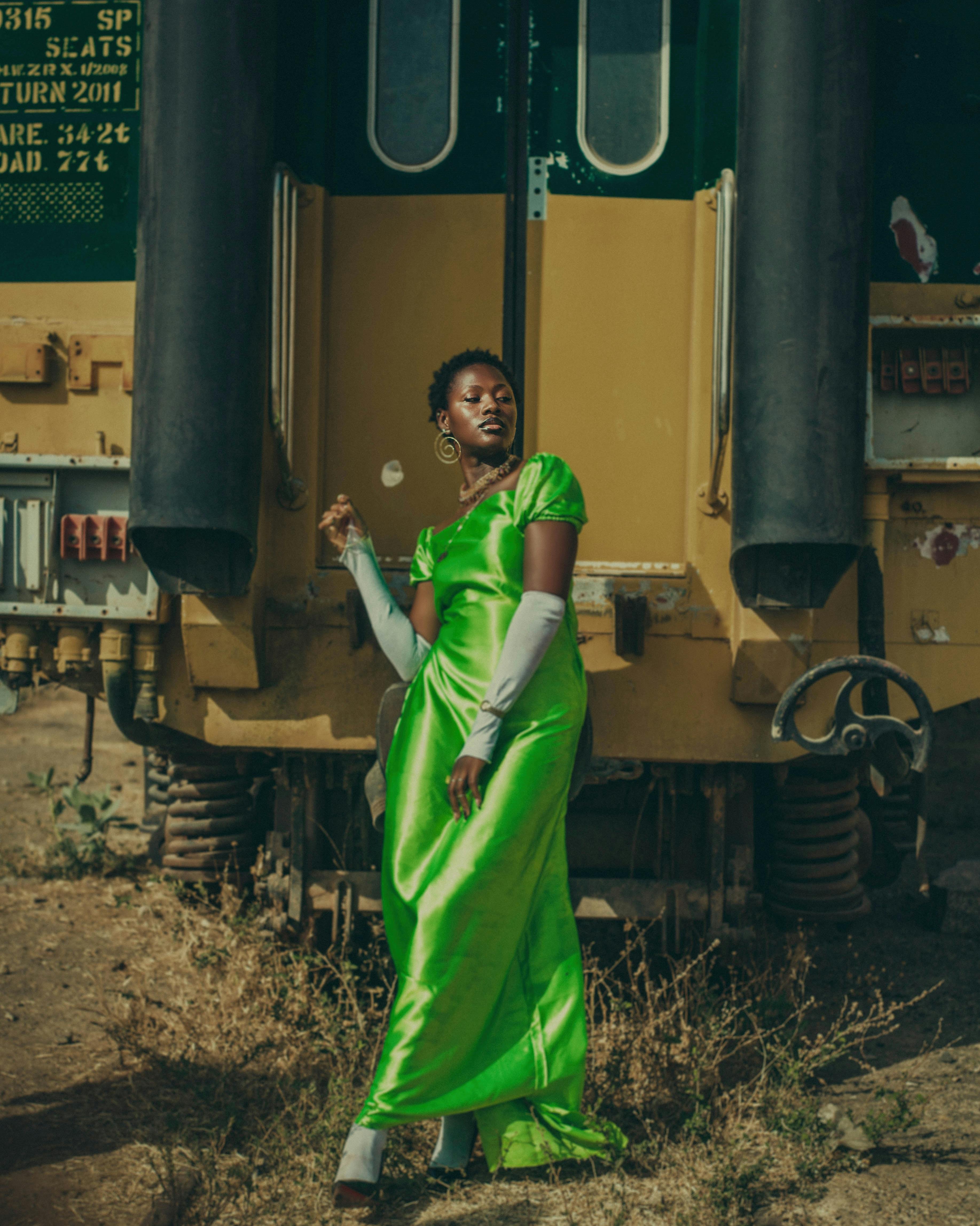 Stylish woman in a vibrant green dress poses confidently near a train.