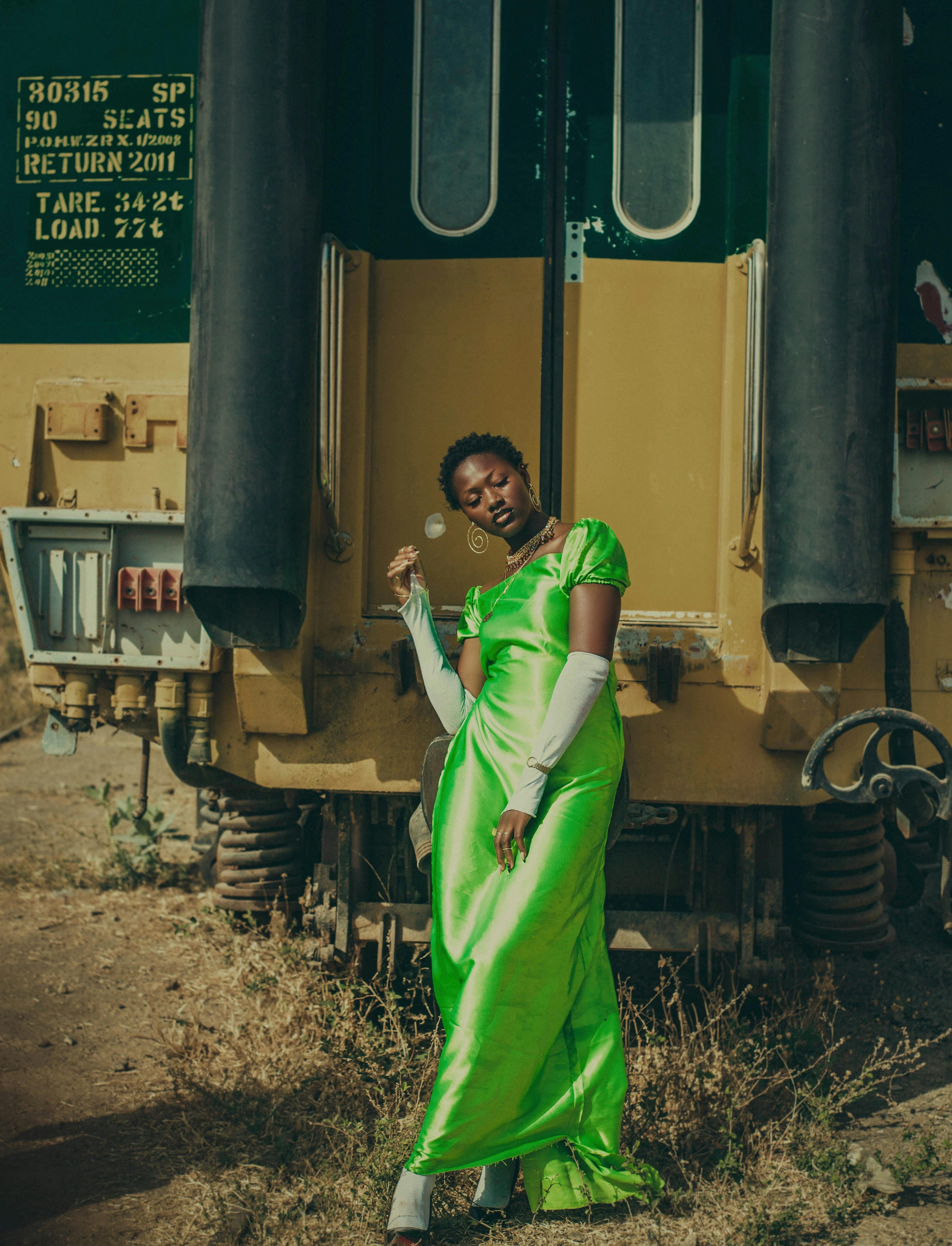 Stylish woman poses in vibrant green dress beside a vintage train outdoors.