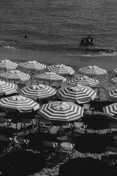 Black and white coastal scene with striped umbrellas and calm ocean waves.