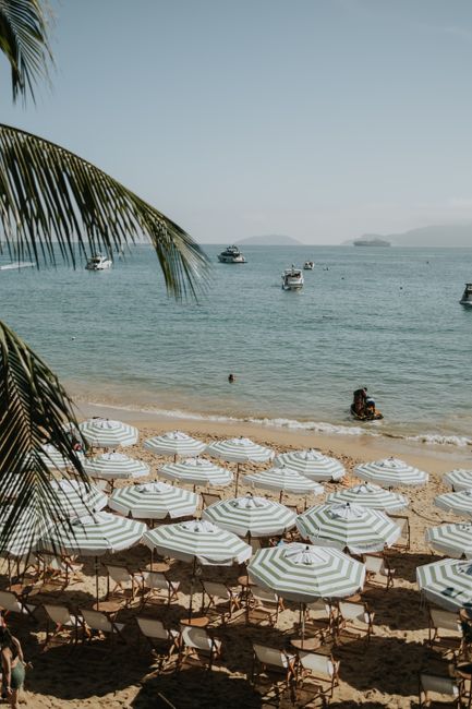 A tranquil beach scene with striped umbrellas and boats on a sunny, clear day.