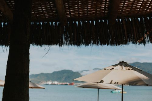 Free Beach scene with umbrellas under a thatched roof overlooking the sea and mountains. Stock Photo