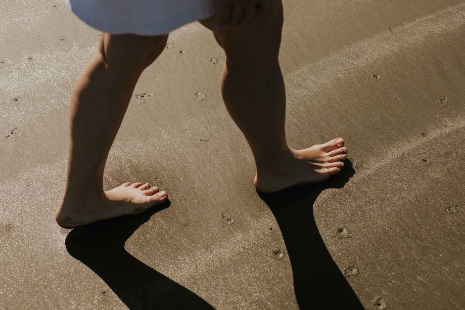 Close-up of a woman's bare feet walking on a sunny beach, casting shadows.