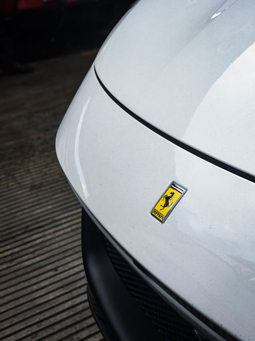 Free Detailed view of a Ferrari emblem on a sleek white car, showcasing luxury and design. Stock Photo