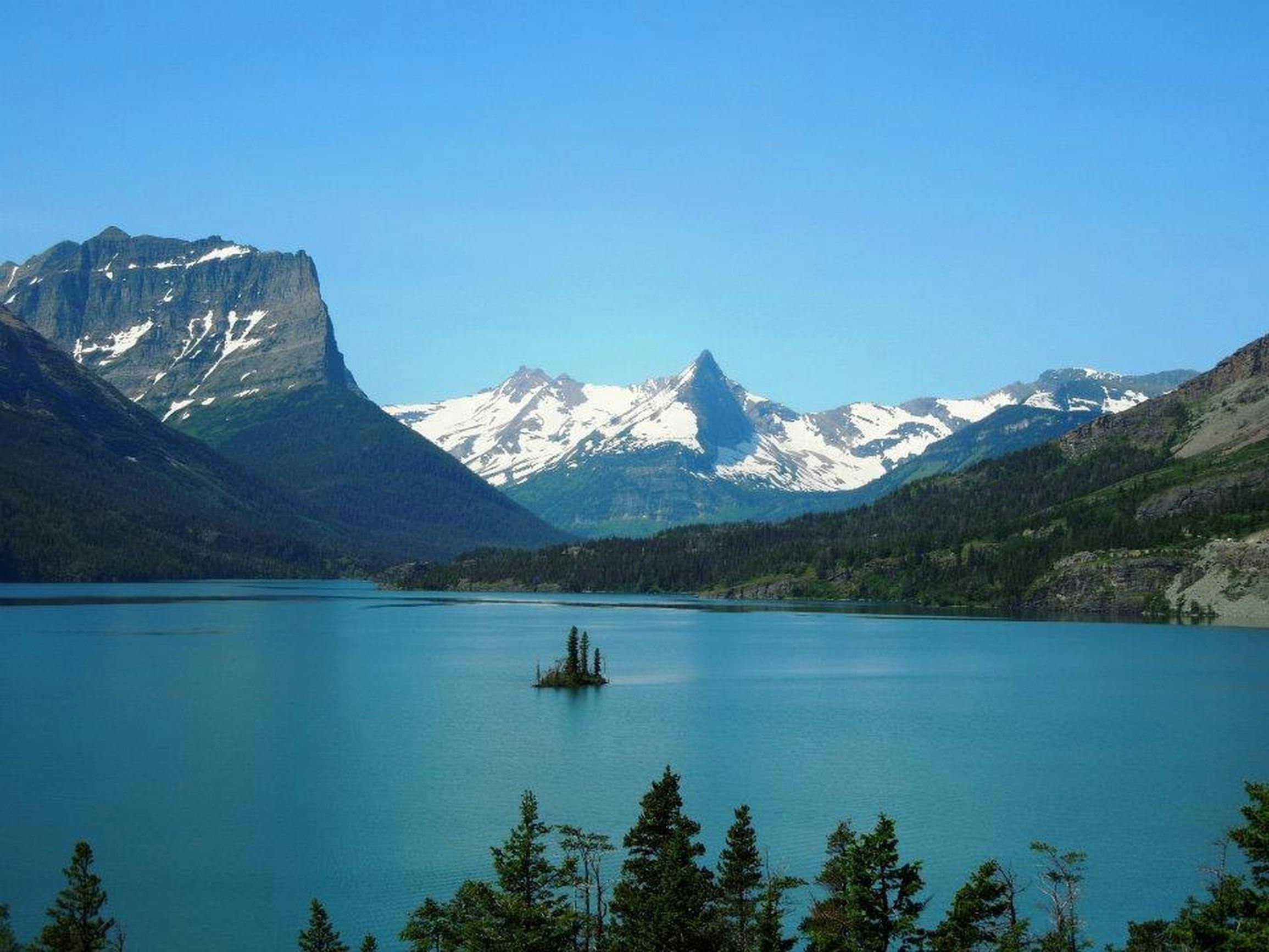Breathtaking view of Glacier National Park with snow-capped mountains and clear lake.