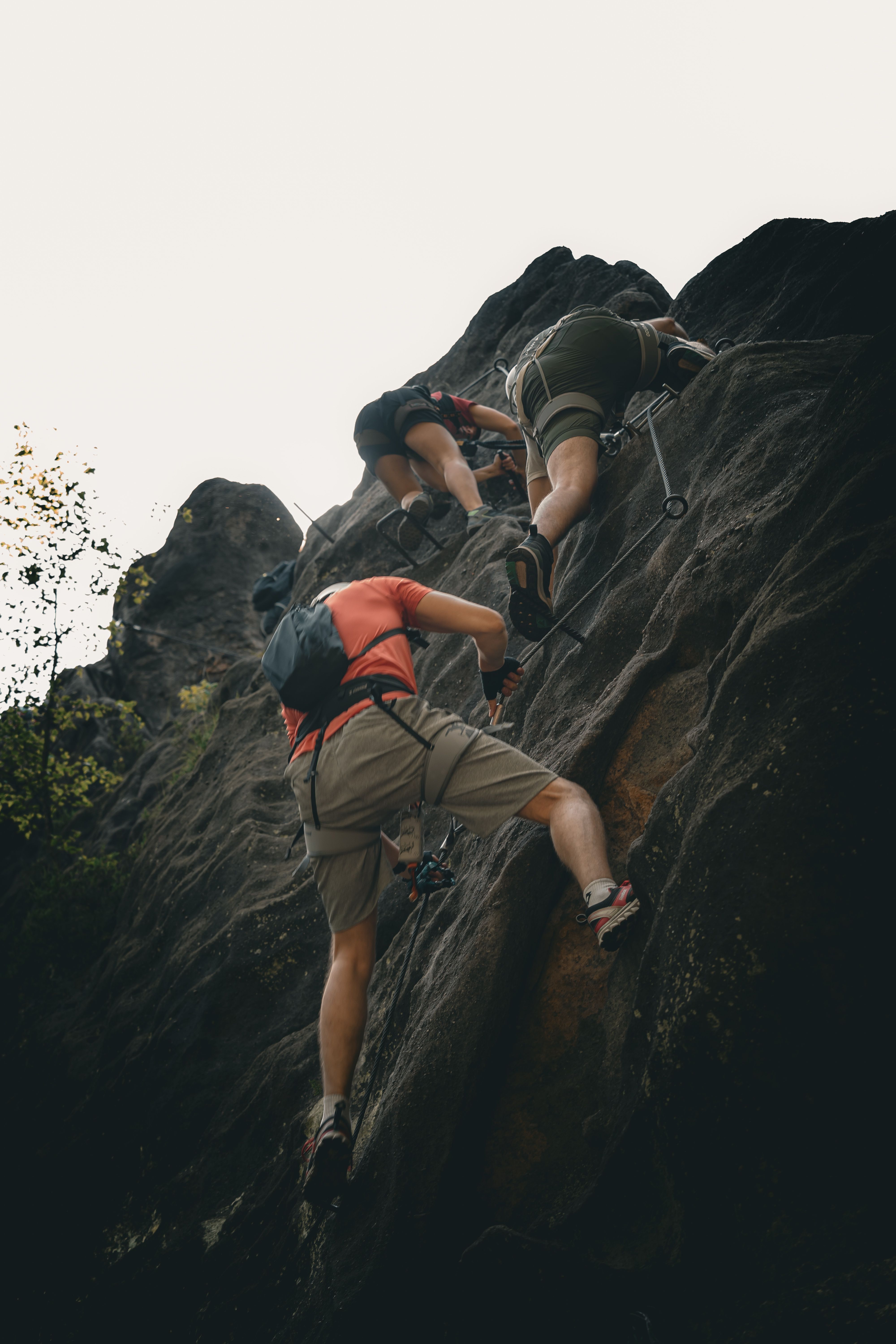 Group of climbers tackling rugged rock face in Oybin, Germany on a cloudy day.