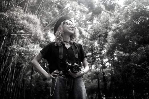 Black and white portrait of a confident photographer with her camera in a lush outdoor setting.