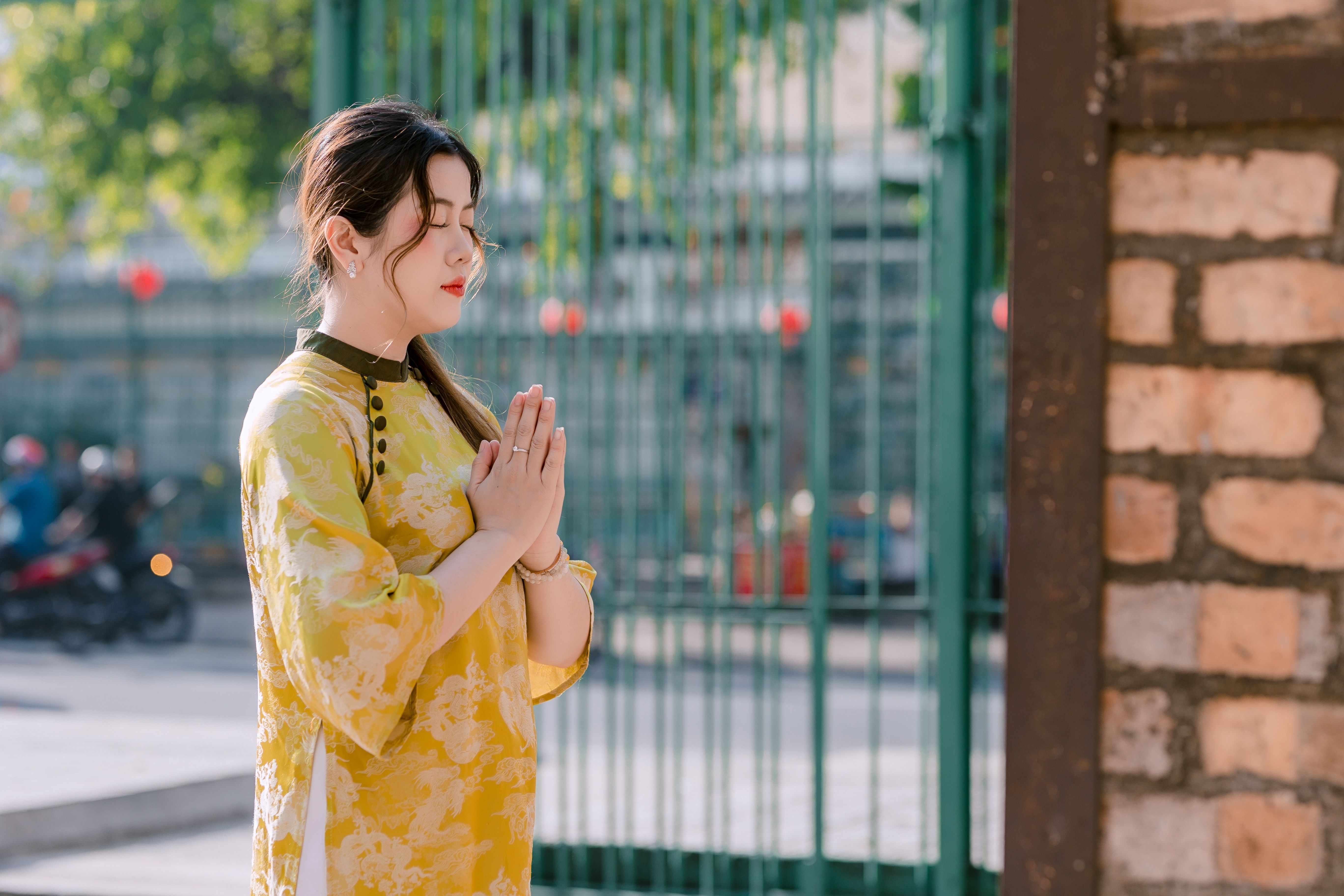 Young woman in traditional yellow dress meditating outdoors by a gate.