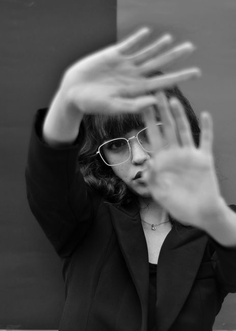 Stylish black and white portrait of a woman in eyeglasses with hands framing face, artistic and modern.