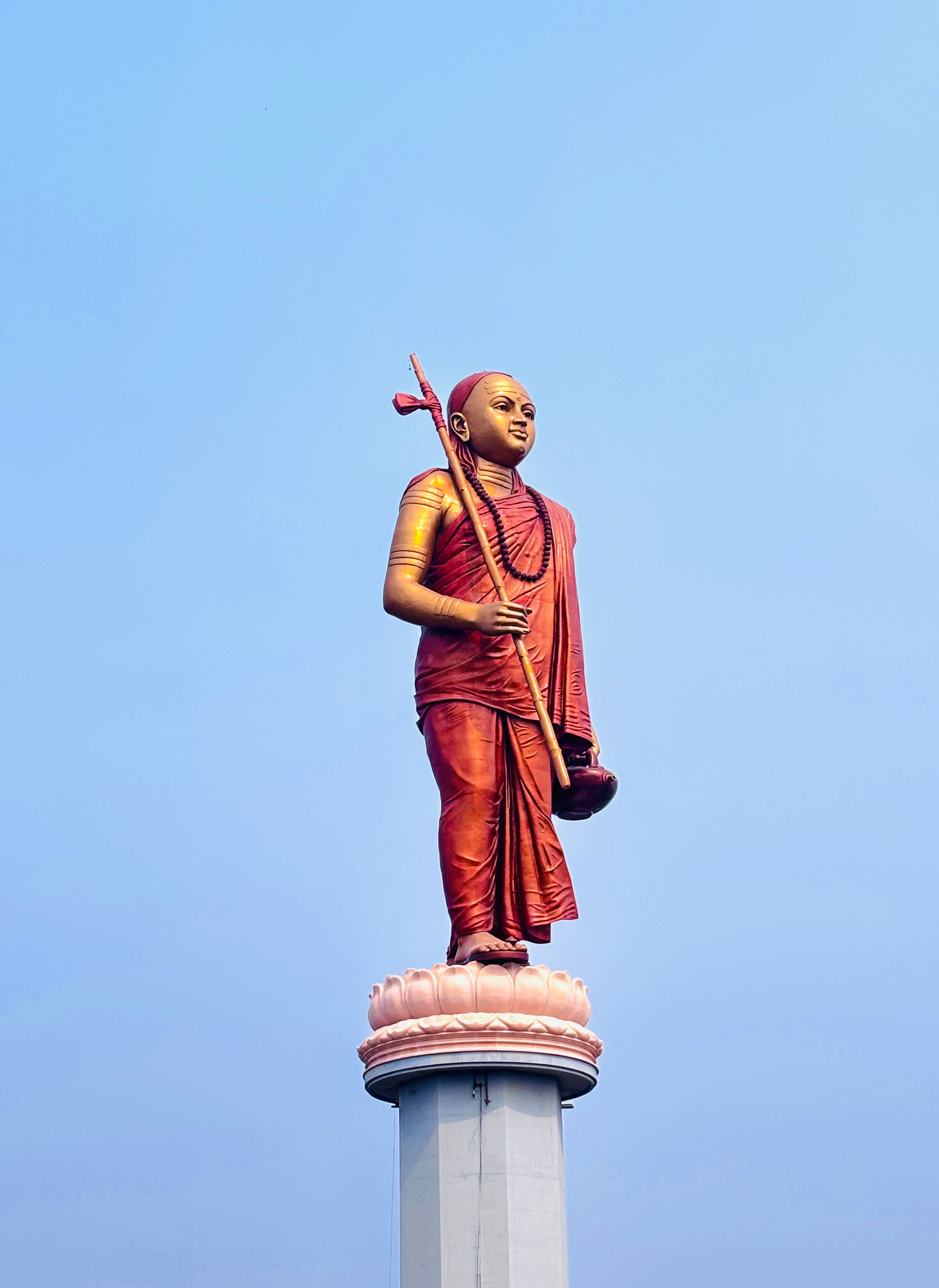 A vibrant statue of a Hindu monk against a clear blue sky in Omkareshwar, India.