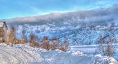 美丽的雪景中，山丘和阴沉的天空下坐落着一座舒适的小屋