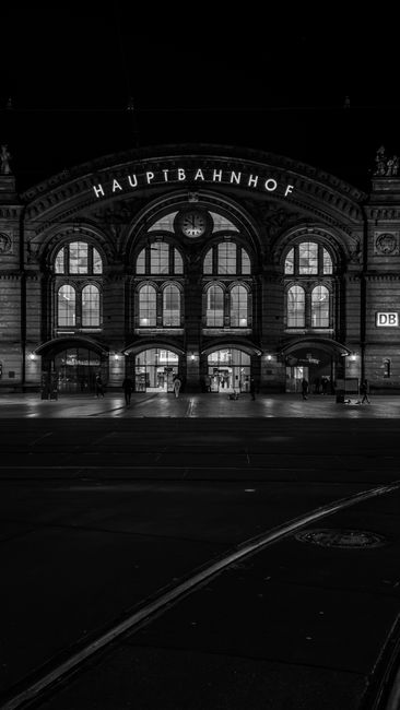 Black and white night photo of Bremen Hauptbahnhof, showcasing its classic architecture under dramatic lighting.
