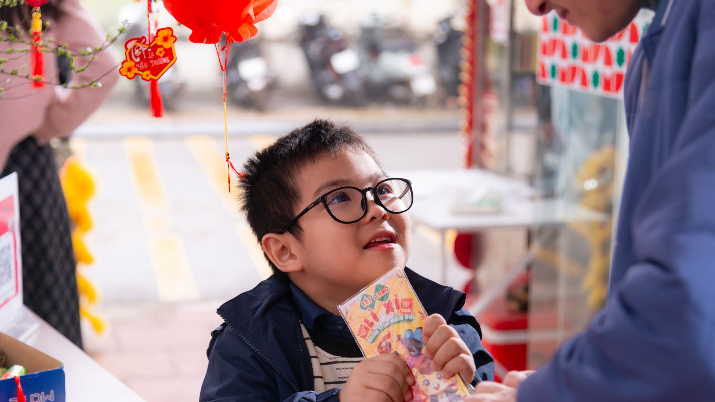 Young boy joyfully receives lucky money envelope during Lunar New Year celebration outdoors.