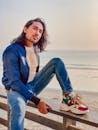 Young man sitting on wooden fence near beach