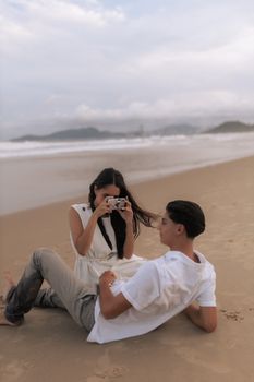 Young couple having a photo session on a sandy beach at sunset, capturing the serene coastal vibe.