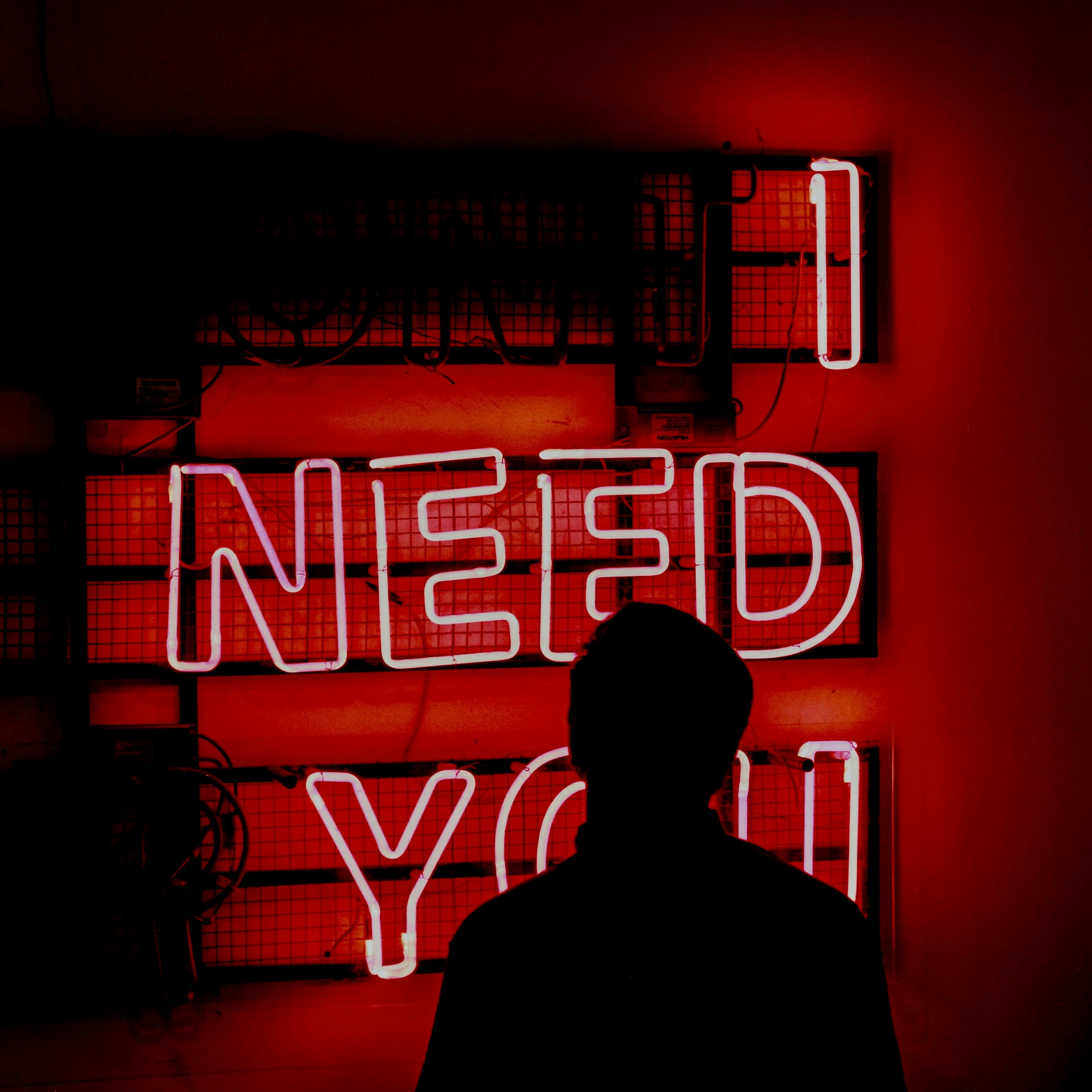 無料 「I Need You」と書かれた赤く輝くネオンサインを背景にした人のシルエット。 写真素材