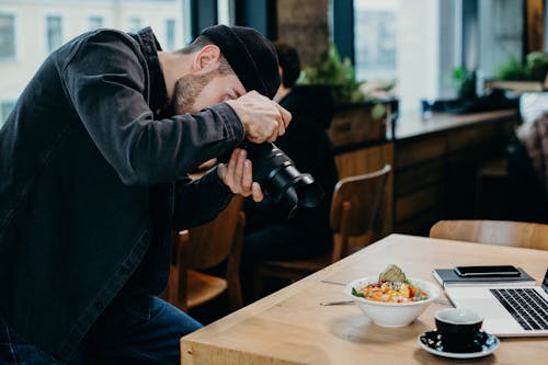 Man Taking Picture of Food on Top of Table Inside Restaurant