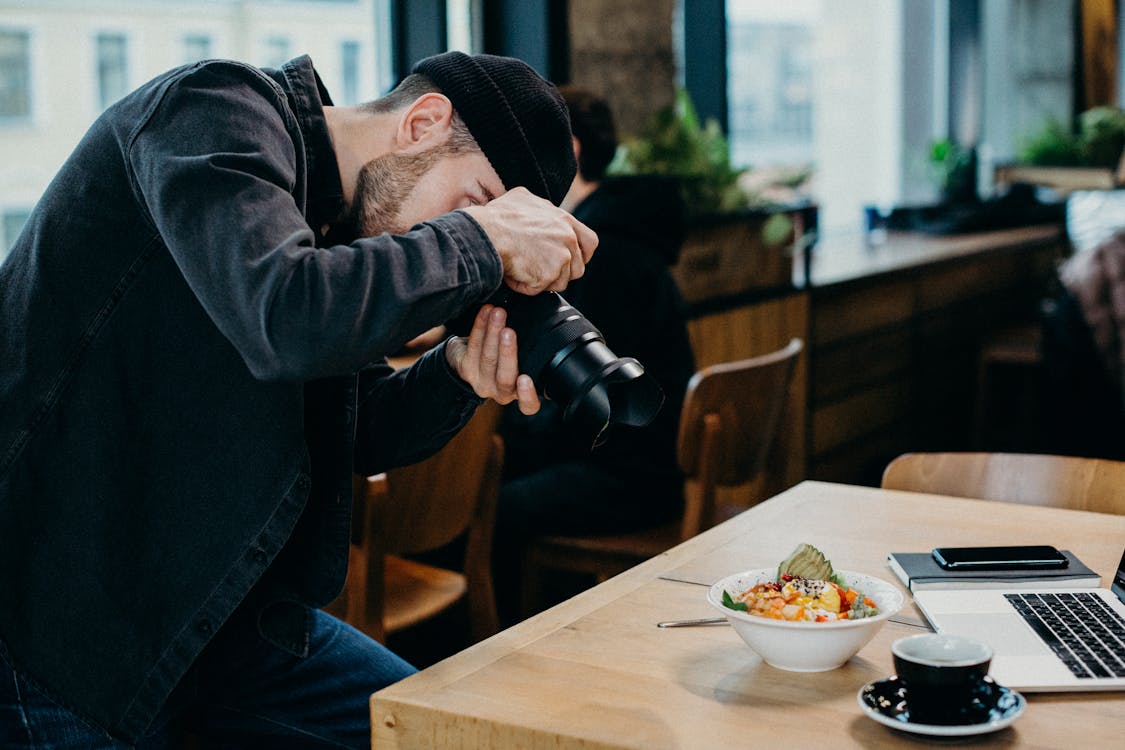 Man Taking Picture of Food on Top of Table Inside Restaurant