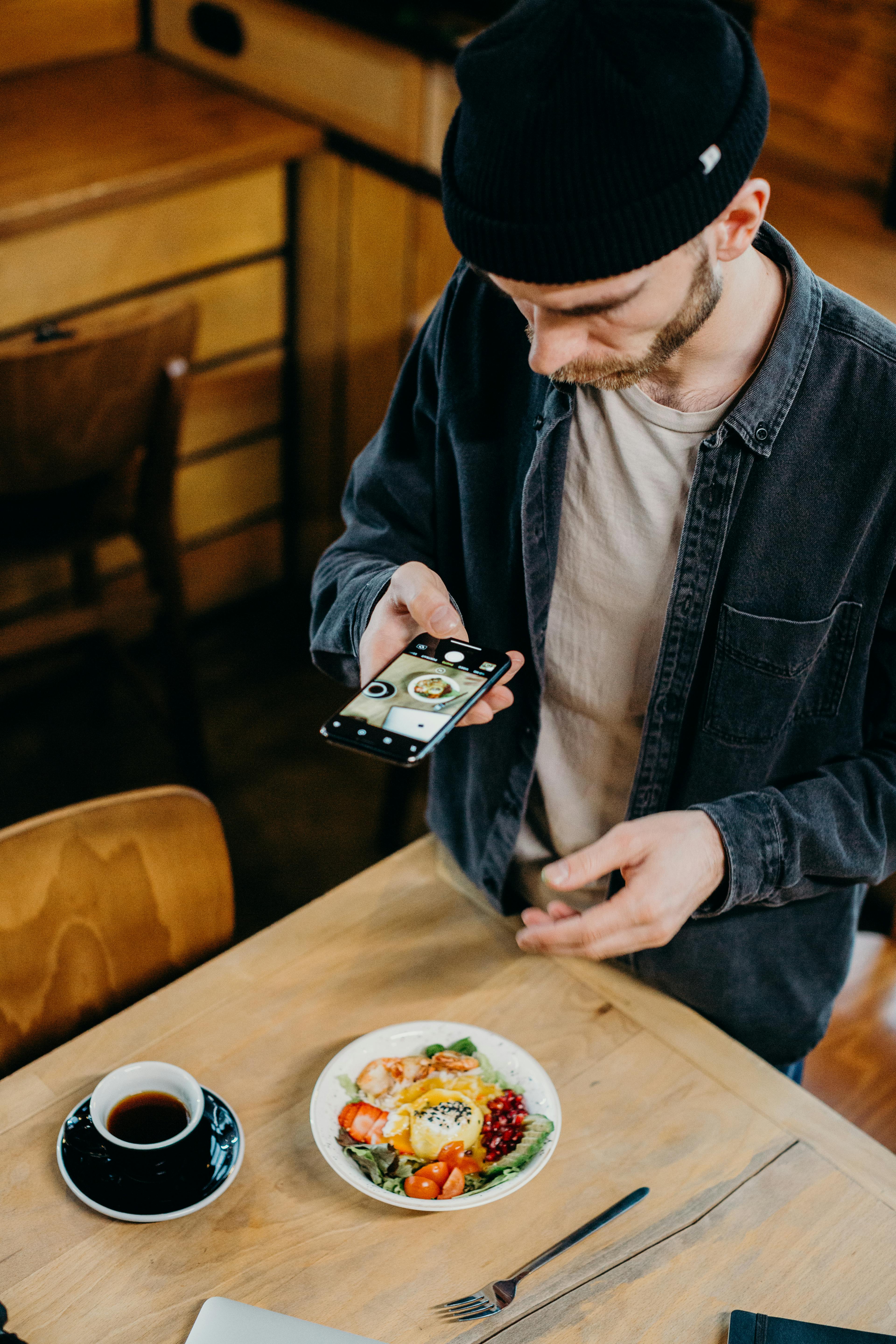 A man photographing his meal with a smartphone in a cozy cafe setting.