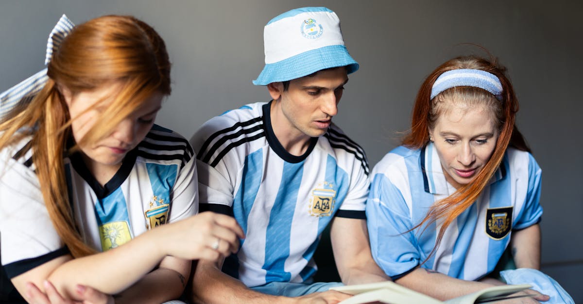 Three fans in Argentina jerseys engage with a book, showing team spirit indoors.