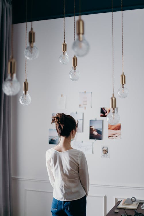 Free Woman Under Pendant Lights Looking at the Photo on the Wall Stock Photo