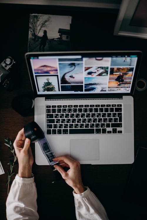 Person Holding and Looking Photo Film at the Table With Macbook Pro