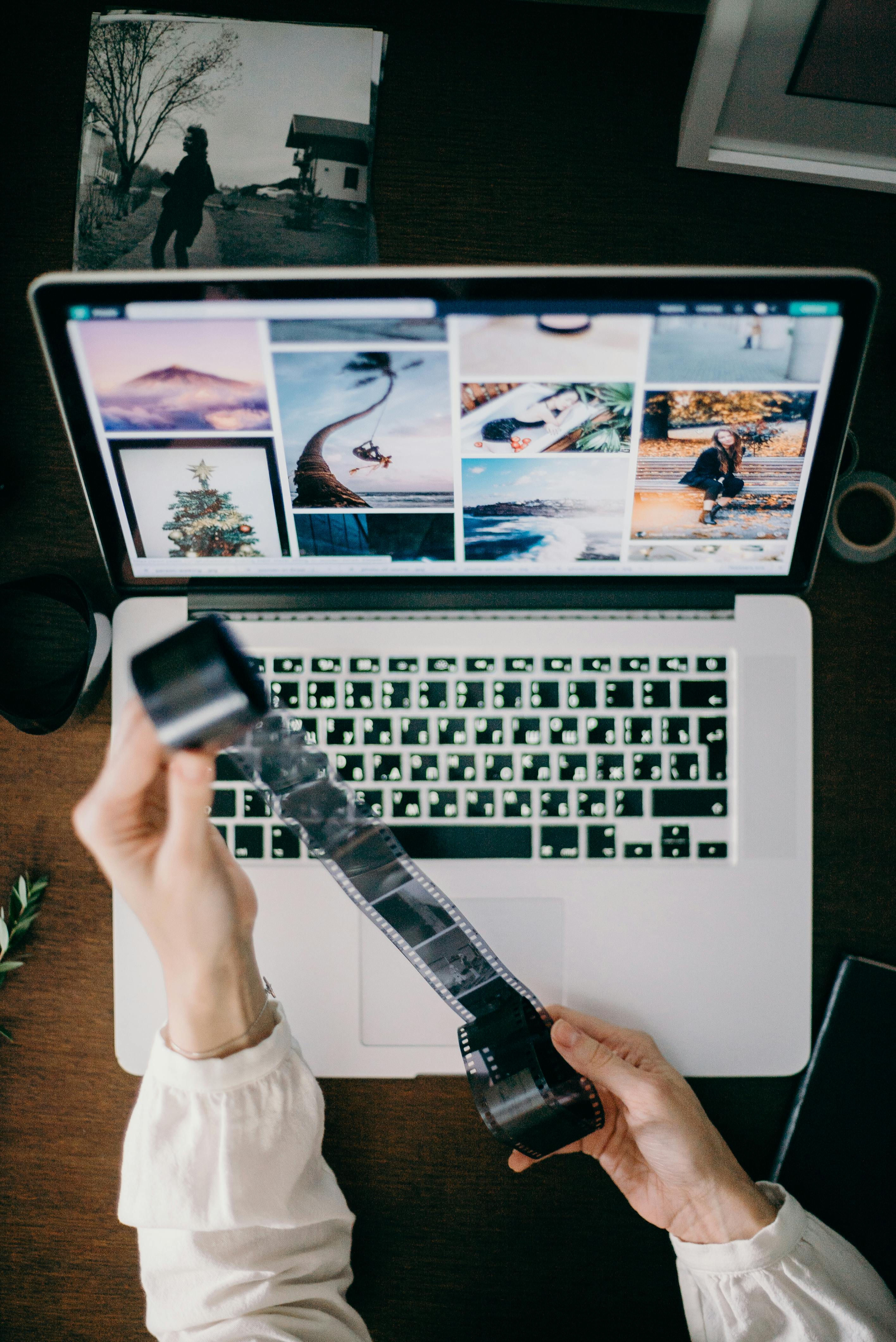 Person holding film strip in front of a laptop. | Photo: Pexels