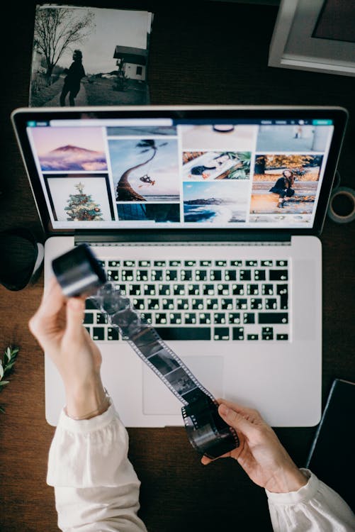 High Angle Photo of Person Holding Film Strip in Front of a Laptop