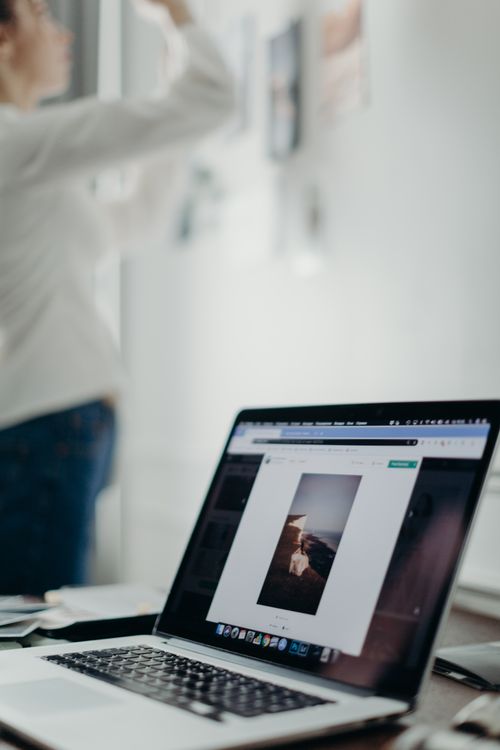 Free A laptop displaying an image with a blurred person arranging art in the background. Stock Photo