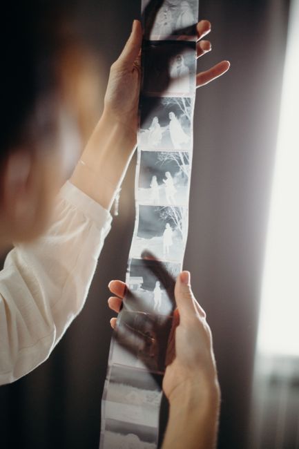 A person holds and examines a photographic film strip indoors with soft lighting.