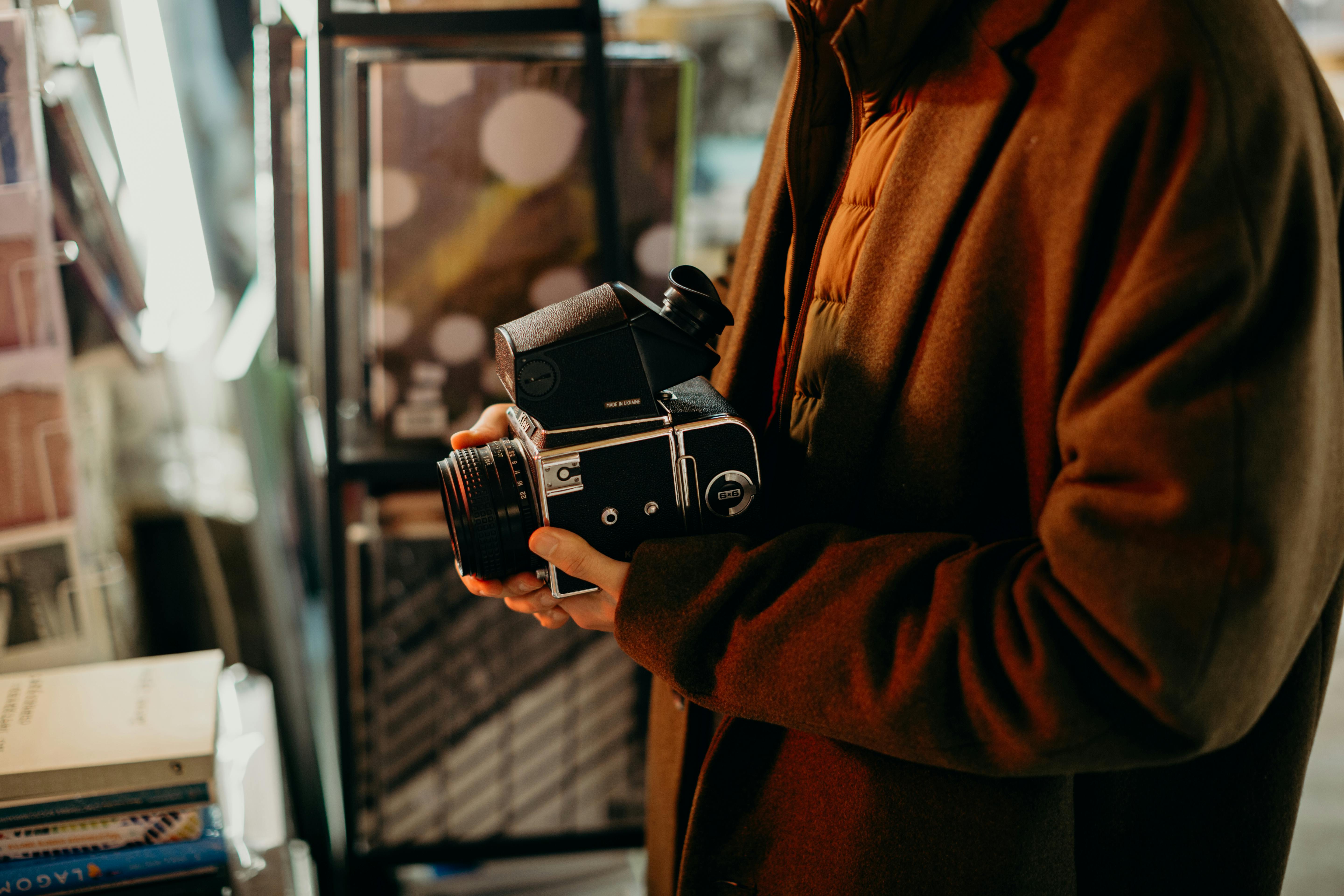 在一家背景模糊的书店里，一个穿着棕色外套的人拿着一台老式相机