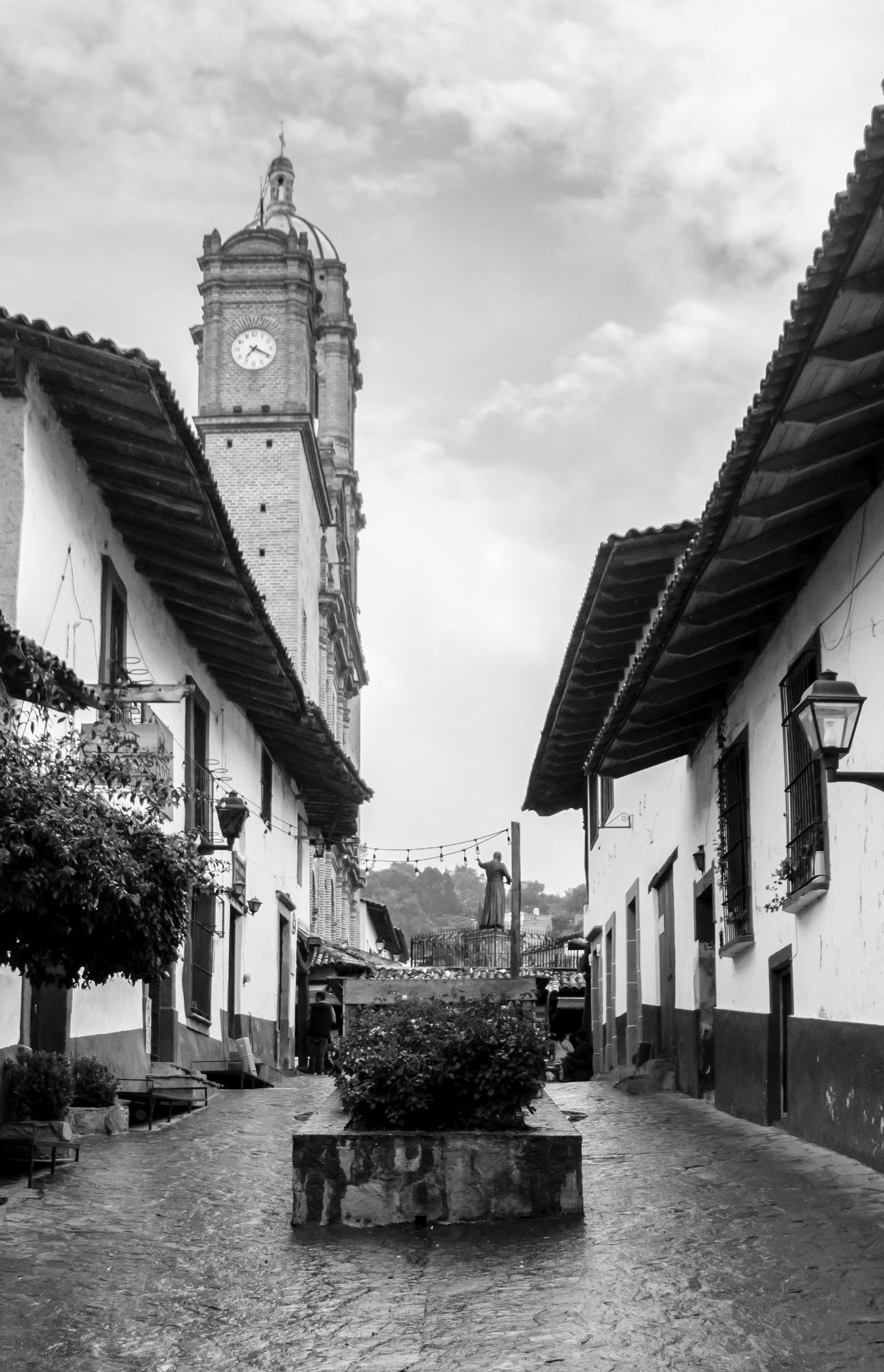 Fotomural Vista en blanco y negro de una torre del reloj histórica y calle de adoquines en un encantador pueblo mexicano.